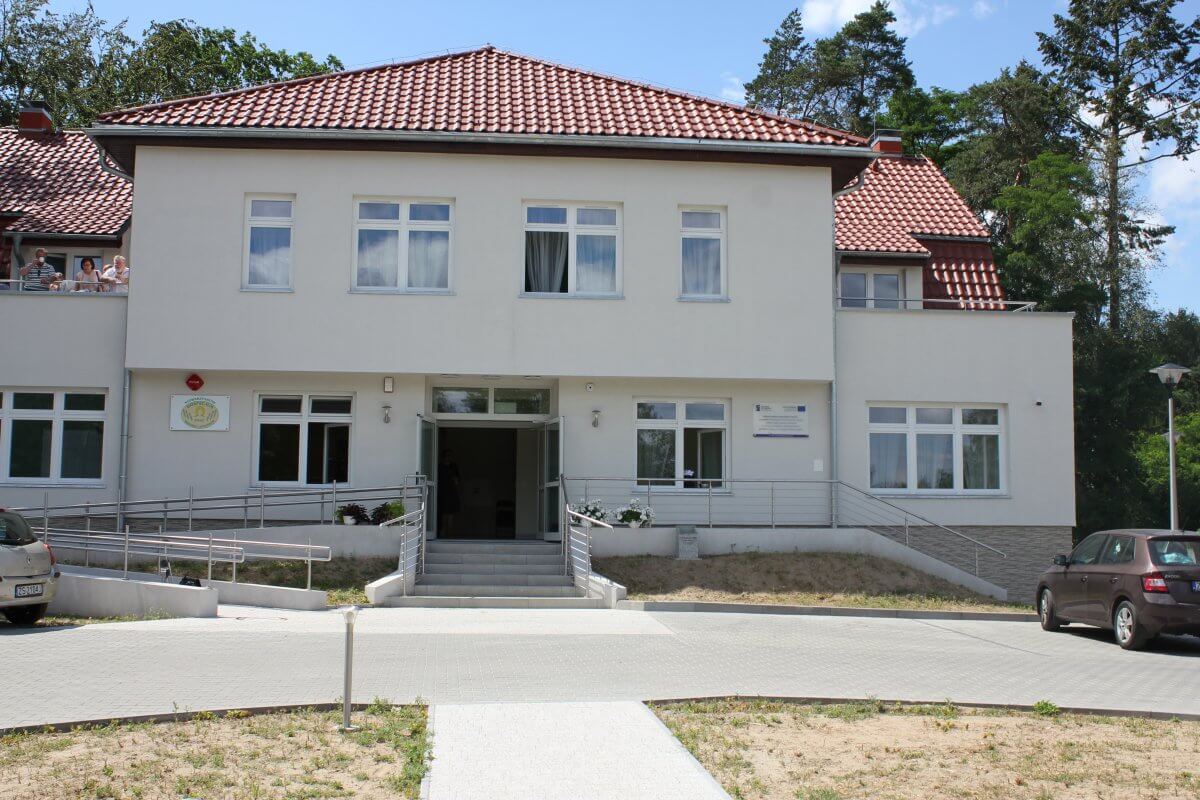 Budynek z czerwoną dachówką, przed wejściem do budynku znajdują się schody i podjazd dla osób niepełnosprawnych