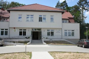 Budynek z czerwoną dachówką, przed wejściem do budynku znajdują się schody i podjazd dla osób niepełnosprawnych