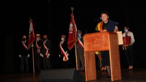 Widać scenę w Miejskim Ośrodku Kultury w Policach, na której przemawia Członek Zarządu Powiatu w Policach. W tle poczty sztandarowe.