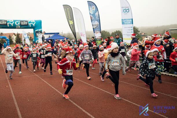 Zdjęcie przedstawia zawodników - dzieci w zawodach biegowych Bieh Mikołajkowy na stadionie lekkoatletycznym w Policach