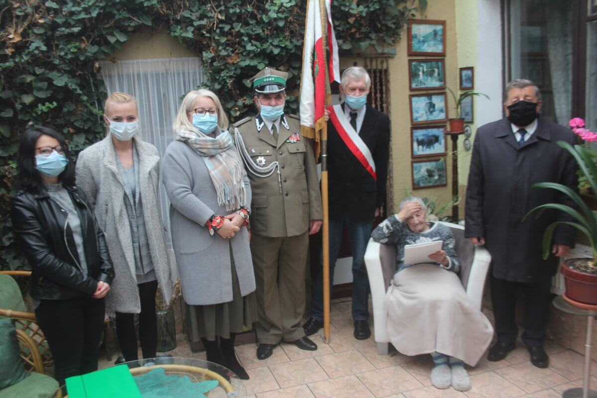 Zdjęcie przedstawia Krystynę Łanowską oraz stojących obok niej po lewej stronie Burmistrza Polic, po prawej stronie Wicestarostę Polickiego oraz przedstawicieli Związku Kombatantów Rzeczypospolitej Polskiej i Byłych Więźniów Politycznych