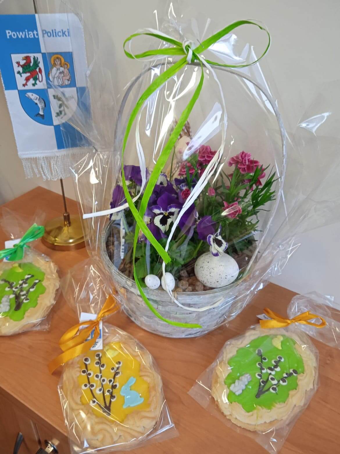 Wielkanocny kosz oraz ozdoby świateczne w postaci 3 kolorowych ciast typu mazurek.