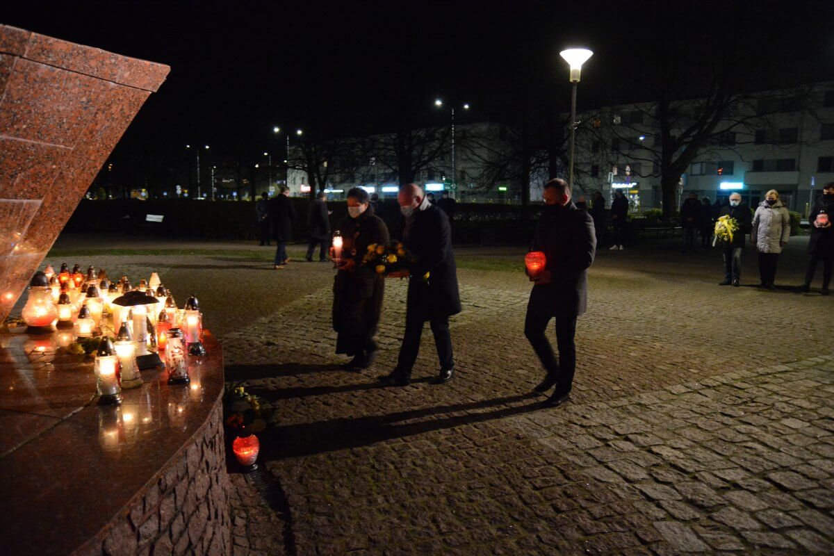 Przewodniczący Rady Powiatu w Policach Cezary Arciszewski, Członek Zarządu Powiatu w Policach Beata Chmielewska oraz Prezes Transnet S.A. Adam Pacholik składają kwiaty i znicze pod figurą św. Jana Pawła II