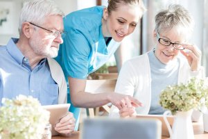 Dwoje seniorów z opiekunem przy urządzeniu mobilnym