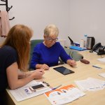 Senior z Powiatu Polickiego przy biurku wraz ze specjalistą rozwiązuje testy na tablecie