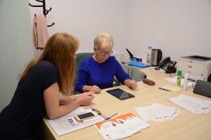 Senior z Powiatu Polickiego przy biurku wraz ze specjalistą rozwiązuje testy na tablecie