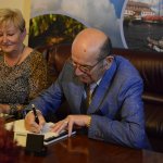 Stefan Marszałek autor książki pt."Oni byli pierwsi" siedzący na skórzanej sofie, podpisujący swoją książkę siedzącej obok pani