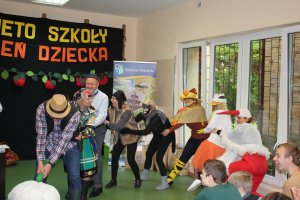 aktorzy przedstawiający scenę wyrywania wielkiej rzepy wspólnymi siłami, w tle napis świeto szkoły i dzień dziecka.