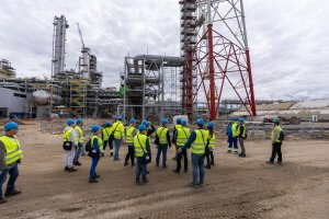 Kilkunastoosobowa grupa przedstawicieli Powiatu Polickiego w trakcie zwiedzania terenu inwestycji wyposażeni w w kamizelki odblaskowe koloru żółtego i niebieskie kaski