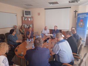 Uczestnicy spotkania, przedstawiciele służb i inspekcji siedzący przy stole w trakcie obrad w siedzibie Państwowej Powiatowej Straży Pożarnejw w Policach