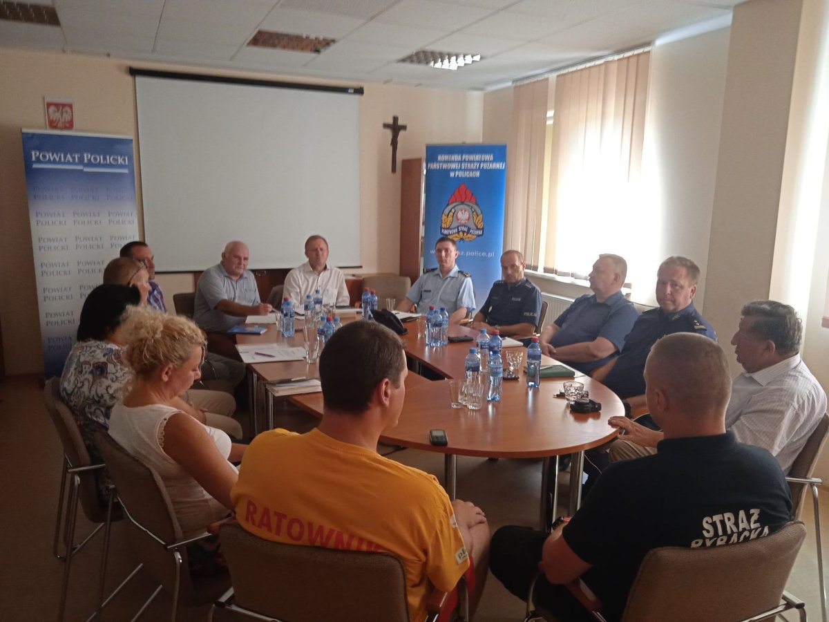 Uczestnicy posiedzenia Powiatowego Centrum Zarządzania Kryzysowego siędzacy przy stole w siedzibie Komendy Państwowej Powiatowej Strazy Pożarnej w Policach