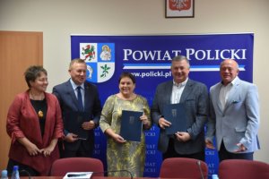 Wspólne zdjęcie przedstawicieli samorządów gminnych i samorządowego na tle granatowej ścianki z herbem i napisami Powiat Policki