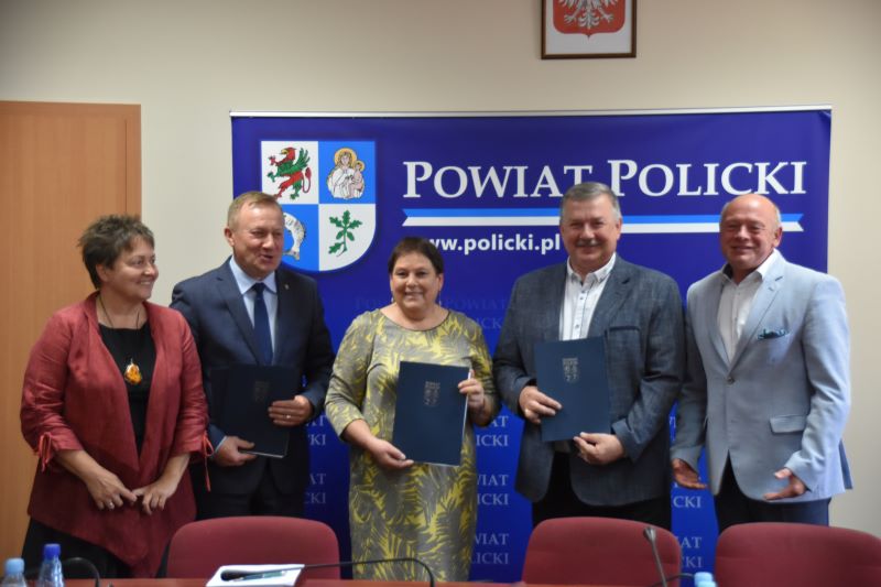 Wspólne zdjęcie przedstawicieli samorządów gminnych i samorządowego na tle granatowej ścianki z herbem i napisami Powiat Policki