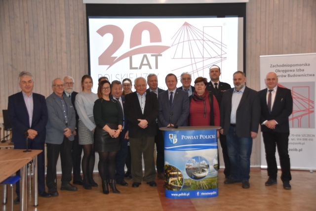 Kilkunasto osobowa grupa uczestników spotkania pozujaca do zdjęcia na tle slaideru z napisem 20 lat Polskiej Izby Inzynierów Budownictwa.