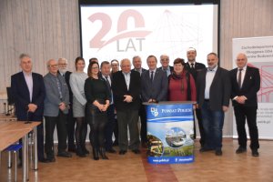 Kilkunasto osobowa grupa uczestników spotkania pozujaca do zdjęcia na tle slaideru z napisem 20 lat Polskiej Izby Inzynierów Budownictwa.