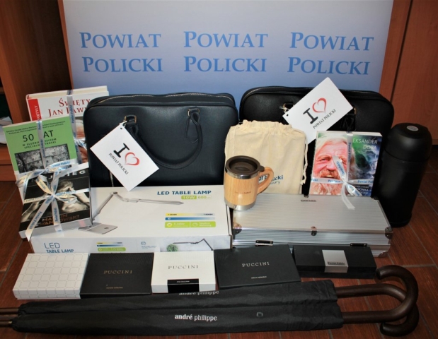 Materiały na licytację: torby i portfele puccini, termos i kubek z logotypem Powiatu Polickiego, zestaw piśmienniczy, zestaw grilowy, zeszyt z ładowarką, lampka biurowa, parasolki, książki takie jak: Marcin Lewandowski Mój Bieg, Święty Jan Pawel II, 50 lat w słuzbie dzieciom specjalnej troski, Na fali i pod prąd Aleksandra Doby