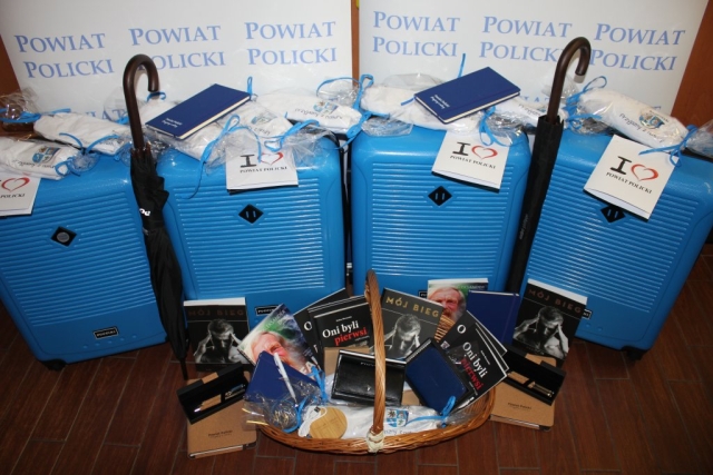 Materiały na licytację, niebieskie walizki puccini, parasolki, książka Aleksandra Doby Na fali i pod prąd, książka Marcina Lewandowskiego Mój bieg oraz dwa zestawy Oni byli pierwsi Stefana Marszałka, notesy Powiatu Polickiego, portfele puccini, zestawy piśmiennicze, koszulki Powiatu oraz ładowarka