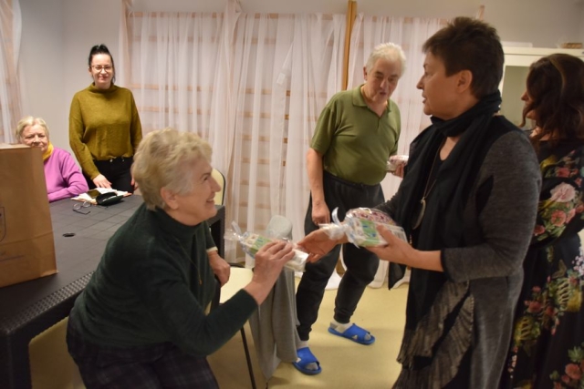 Członek Zarządu Powiatu w Policach Beata Chmielewska wręcza uczestniczce Dziennego Domu Seniora Plus, siedzącej przy stole upominek