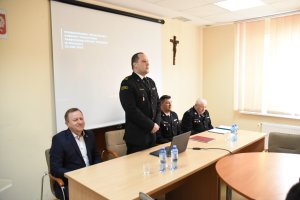 Narada w siedzibie Komendy Powiatowej Straży Pożarnej. Stoi komendant powiatowy, pozostali goście siedzą