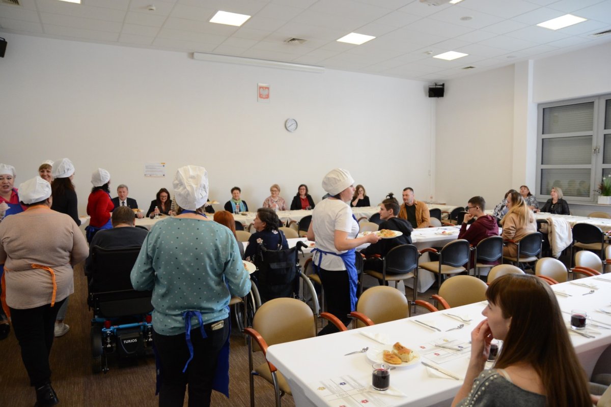 Uczestnicy projektu "Przystanek Police" siedzą przy stole i podają potrawy do stołu