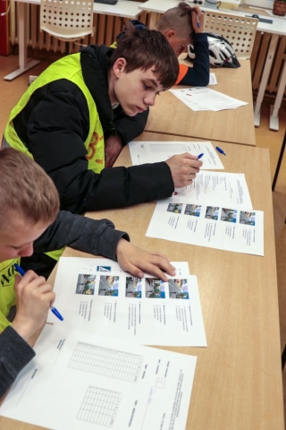 Trzech chłopców w kamizelkach odblaskowych wordu siedzi w ławce rozwiązując test bezpieczeństwa o ruchu drogowym