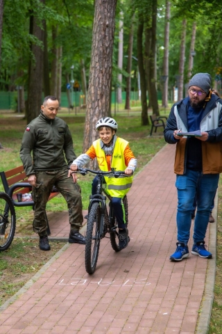Chłopczyk w odblaskowej kamizelce i białym kasku jedzie na rowerze