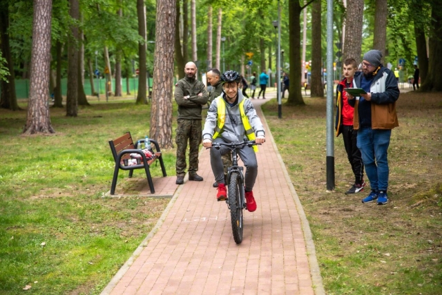 Chłopak w odblaskowej kamizelce i białym kasku jedzie na rowerze, aby pokazać znajomość przepisów ruchu drogowego jako rowerzysta