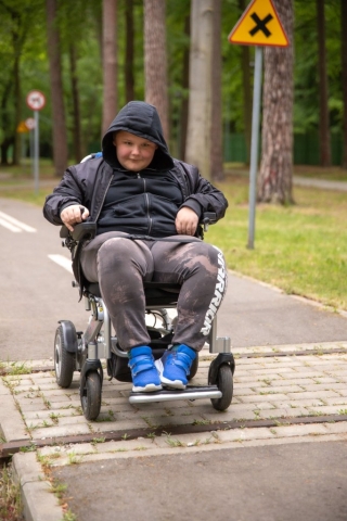 Chłopczyk w ciemnej bluzie poruszający się wózkiem po drodze