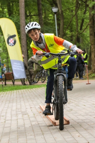 Chłopczyk w kamizelce odblaskowej i białym kasku jeżdżacy na rowerze