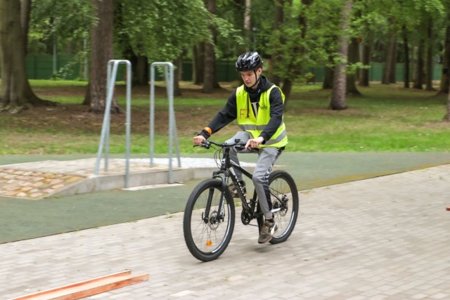 Chłopak w kamizelce odblaskowej i czarnym kasku jeżdżacy na rowerze