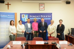 Grupowe zdjęcie samorządowców i wykonawcy pracy na tle reklamy