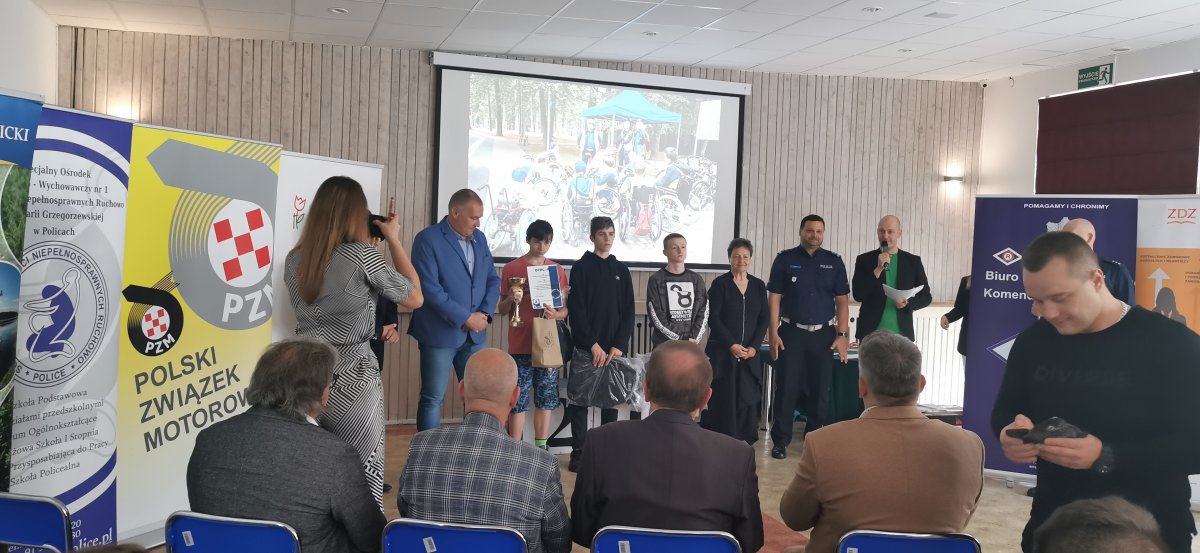 Wyróżnione osoby stoją w tle w jednym rzędzie