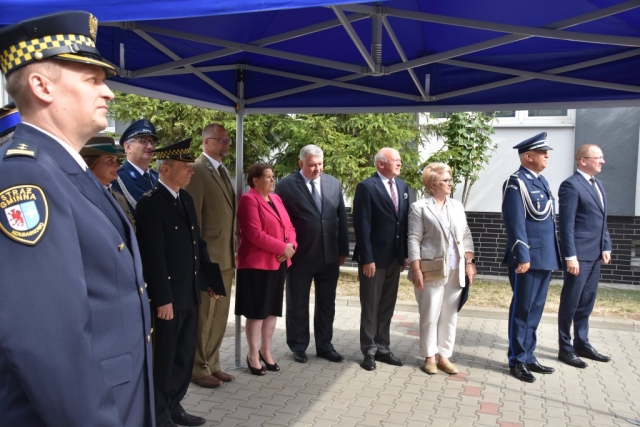 Kilkunastoosobowa grupa mieszana, kobiety, mężczyżni, uczestnicy apelu z okazji Świeta Policji stojący pod zadaszeniem na dziedzińcu komendy.
