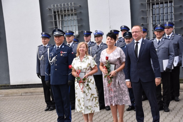Kilkunastoosobowa grupa mieszana, kobiety i mężczyźni przedstawiciele Komendy Powiatowej Policji w Policach, awansowani i wyróżnieni pozujący do zdjęcia na dziedzińcu komendy podczas apelu.