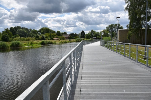 Nurt płynącej rzeki Łarpii, po prawej stronie pomost spacerowy, w tle drzewa i roślinność rzeczna