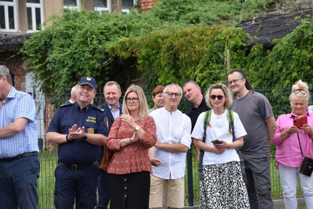 Na tle zielonych koron drzew, stoją zaproszeni goście