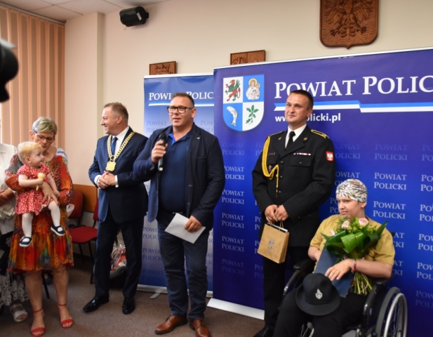 zgromadzenie ludzi, przemowa na ściance do p. Mariki obdarowanej kwiatami, w tle jej bliscy oraz Starosta Policki