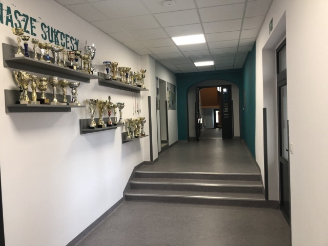 Zdjęcie wewnątrz hali widok holu, na ścianie wiszą złote puchary