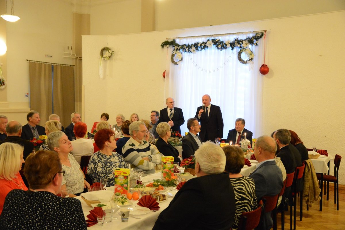 W tle dwóch mężczyzn stojących, z przodu siedzący ludzie