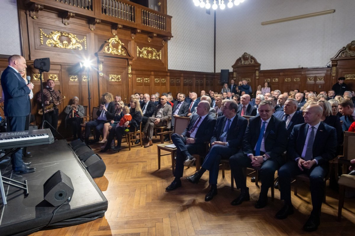 Siedzący goście na dalszym planie.