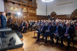 Siedzący goście na dalszym planie.