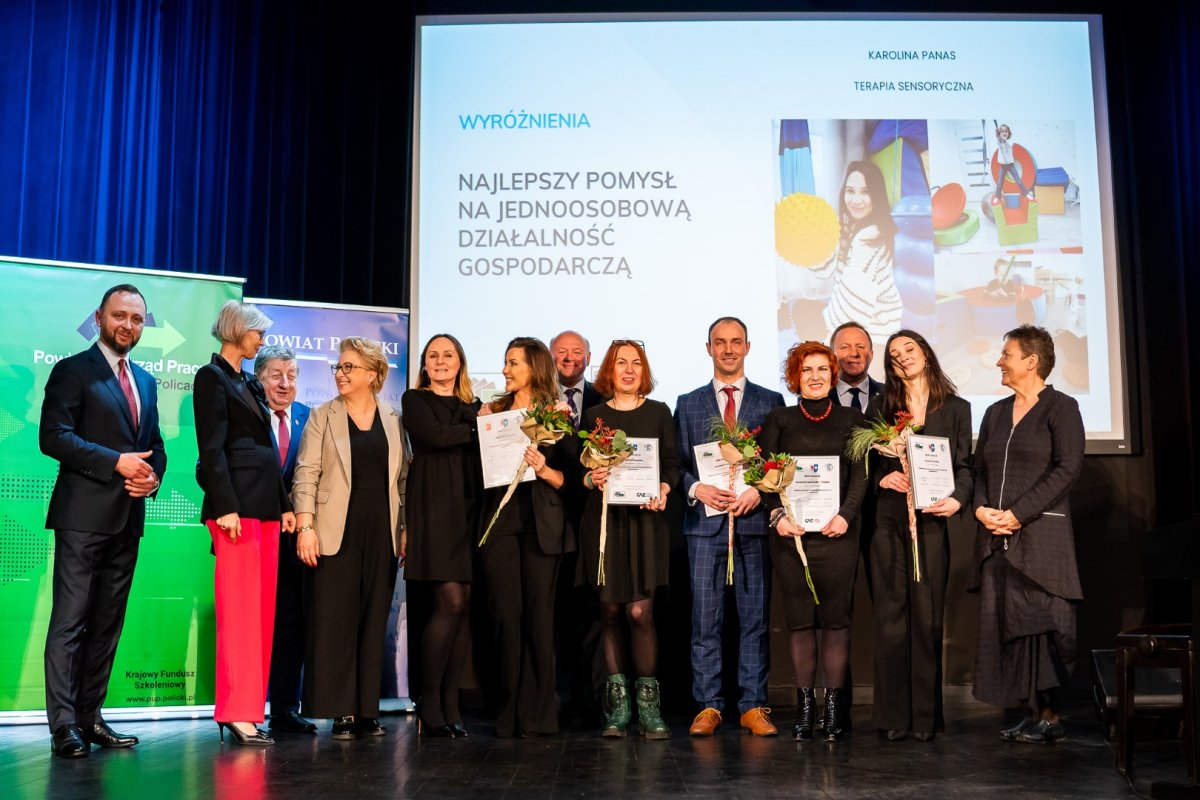 Uczestnicy gali stoją na scenie, w tle prezentacja