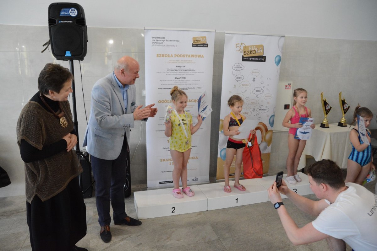 3 osoby stojące na podium, po lewej stronie 2 osoby bijące brawo