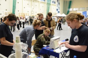 Osoby stojące i siedzące w hali sportowej