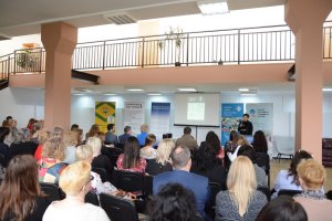 Siedzący ludzie, w tle jedna osoba stoi