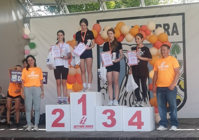 Nagrodzeni uczestnicy biegów stoją na podium otrzymując dyplom medale oraz prezent.