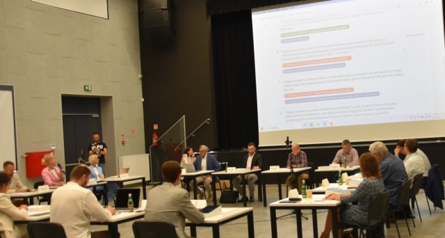 Radni Gminy Kołbaskowo w skupieniu pracują podczas sesji, na wielkim ekranie wyświetlona jest prezentacja.