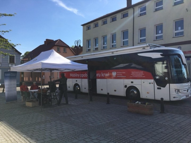 Autobus Mobilnego punktu poboru krwi stojący przy budynku, w tle zabudowania
