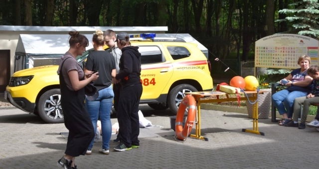 Uczestnicy wydarzenia przechadzający się podczas wydarzenia, w tle widoczny jest samochód Wodnego Ochotniczego Pogotowia Ratunkowego