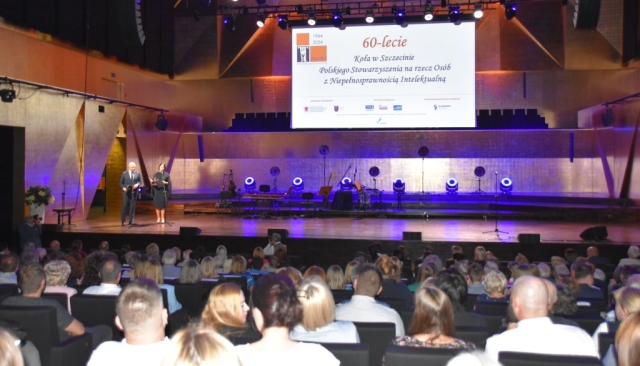 Sala wypełniona goścmi w tle scena i dwoje prowadzących przy mikrofonach